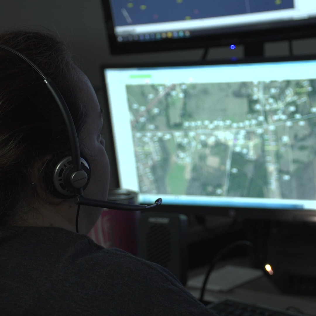 Dispatcher wearing a headset in front of mapping screens